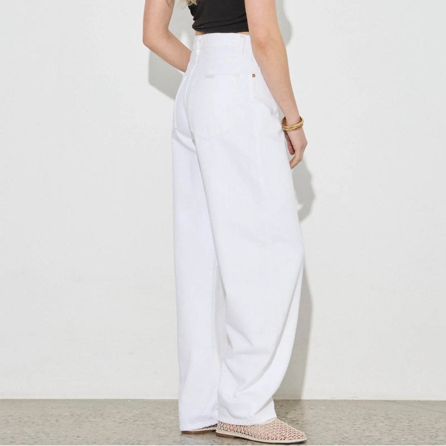 Person wearing a black top and white pants against a white background