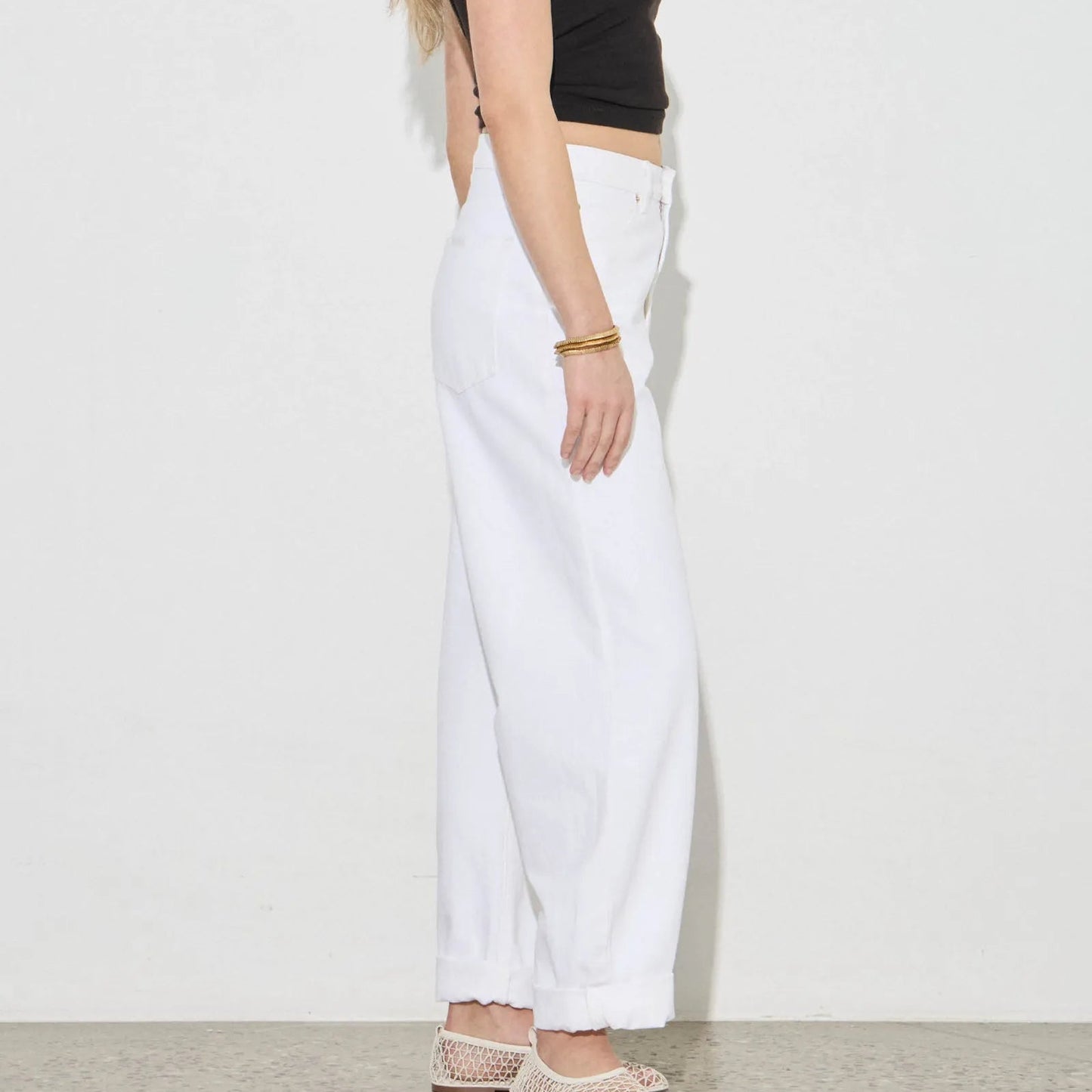 Woman wearing a black crop top and white pants against a plain background