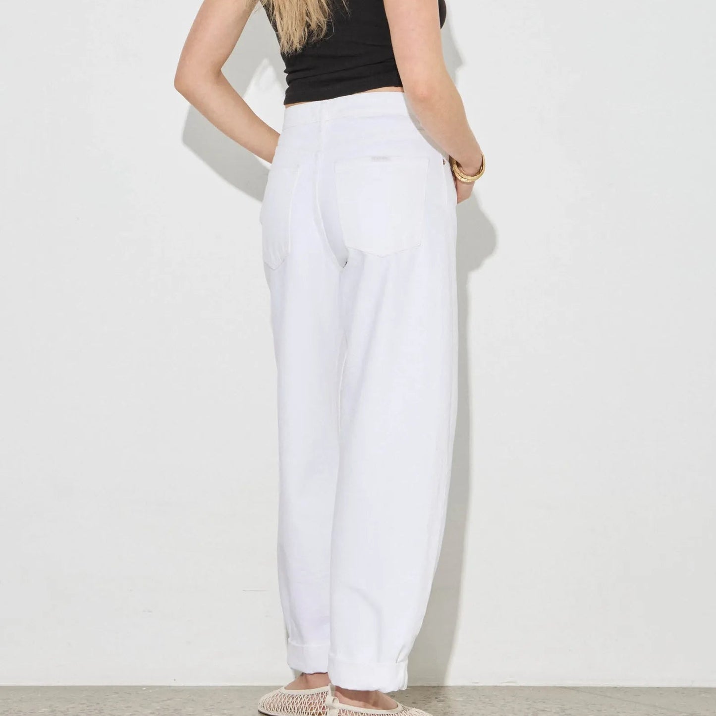 Woman wearing a black top and white pants against a plain background